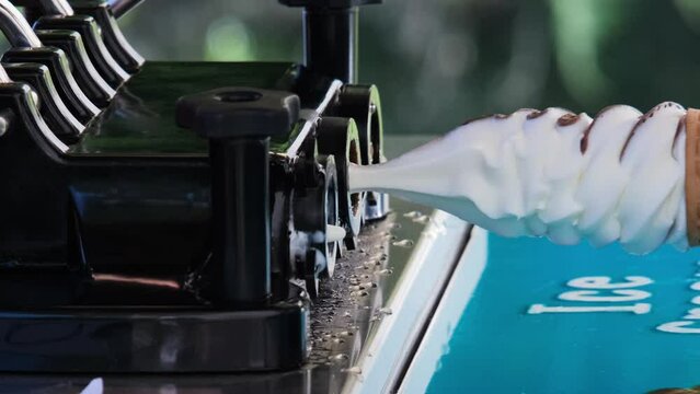 Vertical video. Close-up of female seller making soft serve ice cream from machine outdoors. Takeaway food and summer season concept