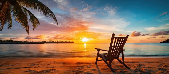 Beach chair with palm tree and sea at sunrise - vacation concept.