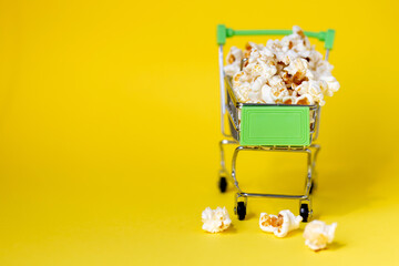 Freshly made popcorn on yellow background in a shopping cart