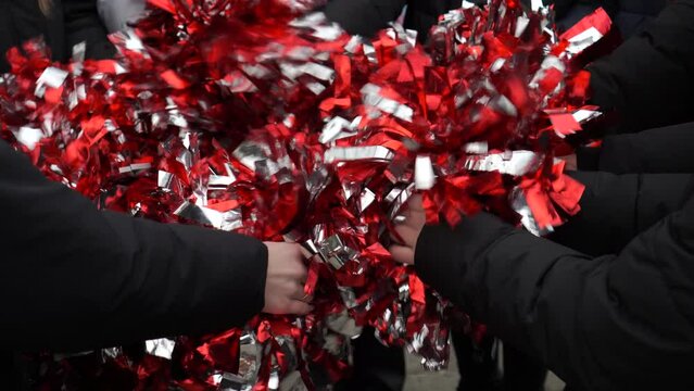 the hands of the girls with sleeves in a black jacket and pompoms made of shiny tinsel in red and silver colors