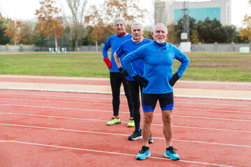 Three senior male runners show determination on a running track, dressed in blue athletic gear,...