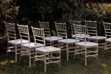 Fototapeta na wymiar Row of elegant, transparent chairs with white cushions set outdoors in soft sunlight. Concept: outdoor events, modern design, or garden parties. Plenty of copy space.