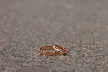 Two golden wedding bands, simple and without gemstones, are placed closely together on a textured...