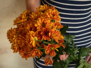 A horizontal close up of a woman in a striped dress holding a bunch of orange chrysanthemums.