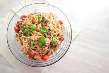 Cold spaghetti salad with tomatoes, arugula, mozzarella, olives and a creamy dressing with basil garnish in a glass bowl on a white painted table, top view from above, copy space