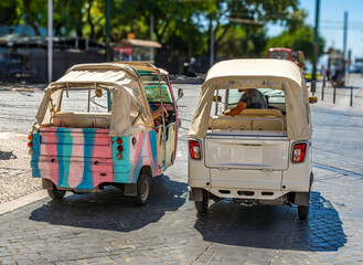 Two Piaggio Ape Calessino 200 three-wheeled tourist Tuk tuks parked on a cobblestone street in Lisbon in Portugal with tram tracks on the ground.