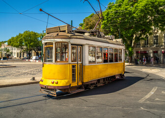 Famous and typical old yellow Portuguese tram, beautifully decorated and preserved, running on the tracks of a roundabout of a typical Lisbon street in Portugal.