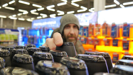 Close-up of many black plastic bottles of shampoo or shower gel and a male buyer taking one