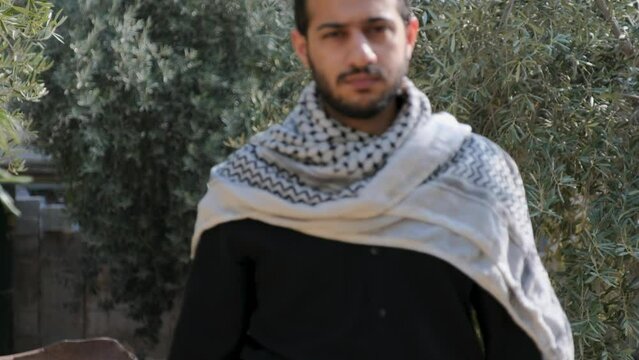male wearing keffiyeh in olive tree field with angry look on his face and victory
