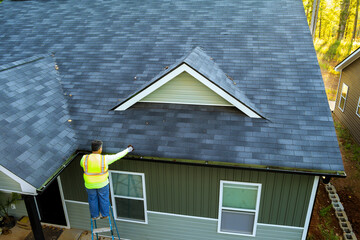 Using ladder, worker cleans debris, dirt, fallen leaves from clogged roof gutter drain