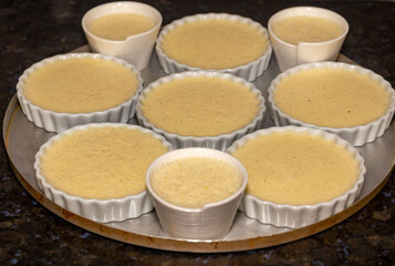Creme brulee in white ramekins lined with white spoons on rustic background with shallow depth of field blur.