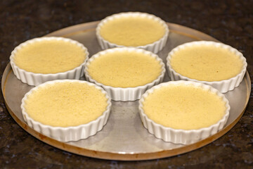 Creme brulee in white ramekins lined with white spoons on rustic background with shallow depth of field blur.