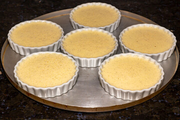 Creme brulee in white ramekins lined with white spoons on rustic background with shallow depth of field blur.