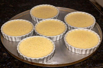 Creme brulee in white ramekins lined with white spoons on rustic background with shallow depth of field blur.