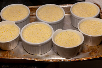 Creme brulee in white ramekins lined with white spoons on rustic background with shallow depth of field blur.