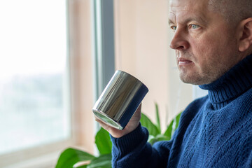 Portrait of the mid aged man with grey hair, wearing warm, dark blue sweater, drinking coffee....