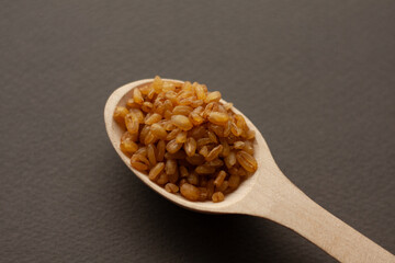 bulgur grains in a wooden spoon on a dark background