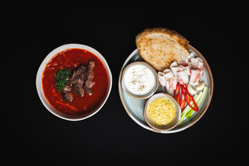 Ukrainian borscht with meat, lard, onion, pepper and mustard on a black background.