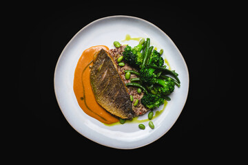 Golden fish fillet with vegetables on a black background.