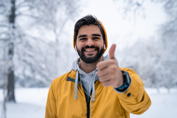 Satisfied smiling handsome man with beard looking at camera with thumb up standing outdoors in...