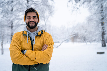 Fototapeta na wymiar Portrait photo of cheerful attractive man with arms crossed standing in woods on cold snowy winter day.