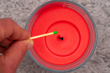 red wax candle with green headed matchstick approaching the wick.