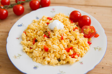 Leckeres Frühstück, Rührei mit Tomaten und Paprika auf einem weißen Blumenteller auf einem rustikalen Holztisch