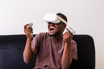 young man wearing a vr headset engrossed in a virtual reality game and holding controllers sitting...
