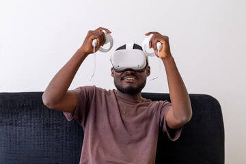 young man wearing a vr headset engrossed in a virtual reality game and holding controllers sitting...