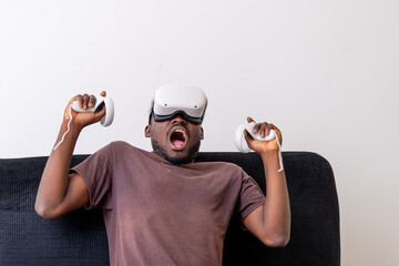 young man wearing a vr headset engrossed in a virtual reality game and holding controllers sitting on a couch. Vr gaming concept