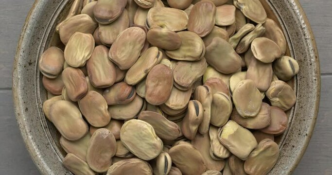Top view oof whole dry Fava Bean (Vicia faba) in a bowl on a wooden table, rotating in a circle. 