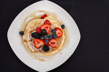 Stack of pancakes on a plate with fresh blueberries and strawberries
