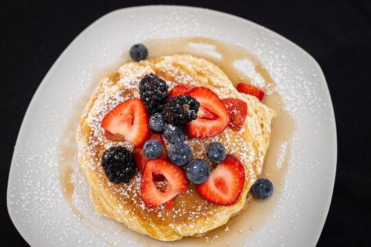 Stack of pancakes on a plate with fresh blueberries and strawberries
