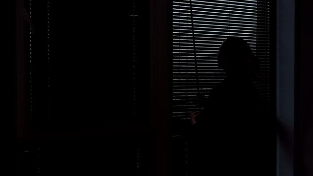 Silhouette of a woman opening the blinds. Wooden blinds that open on large windows in the interior.