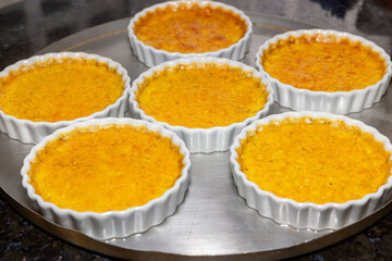 Creme brulee in white ramekins lined with white spoons on rustic background with shallow depth of field blur.