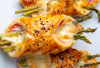 Baked green asparagus with ham and cheese in puff pastry sprinkled with sesame seeds and green basil leaves.