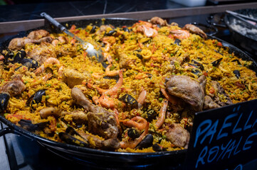 Street food in France, fresh prepared colorful paella with rice and sea food in big pan on street...
