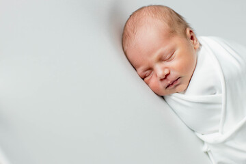A 3-day-old baby wrapped in white cloth sleeping on a white background