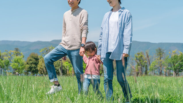 空の見える公園で手を繋いでジャンプして遊ぶ子供と両親のアジア人家族・ファミリーイメージ
