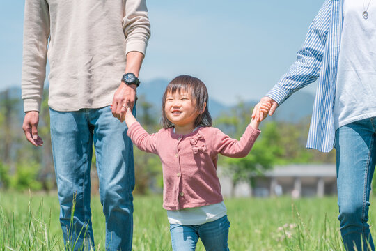 空の見える公園で手を繋いでジャンプして遊ぶ子供と両親のアジア人家族・ファミリーイメージ

