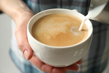 Woman pouring milk into cup of hot coffee, closeup