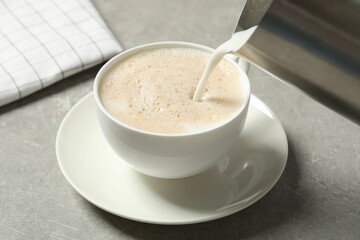 Pouring milk into cup of coffee on grey table