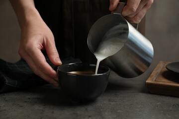 Woman pouring milk into cup of coffee at grey table, closeup