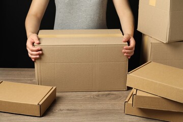 Packaging goods. Woman with cardboard boxes at wooden table, closeup