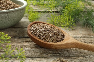 Spoon with dry seeds and fresh dill on wooden table, closeup