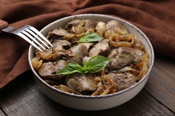 Delicious fried chicken liver with onion and basil in bowl on wooden table, closeup