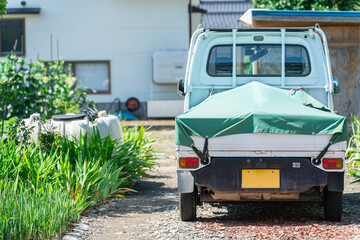 田舎の家に駐車しているカバー付き軽トラック
