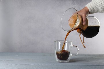 Woman pouring tasty drip coffee into cup at grey wooden table, closeup. Space for text