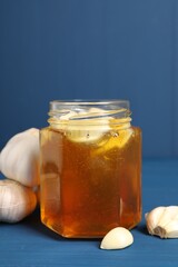 Honey with garlic in glass jar on blue wooden table