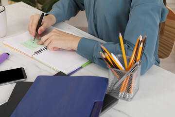 Woman writing on sticky note at white marble table indoors, closeup